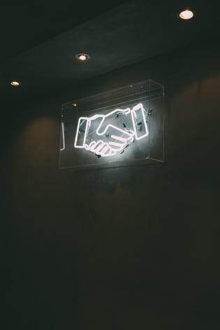 Weisses Neonschild "Händedruck" an Wand